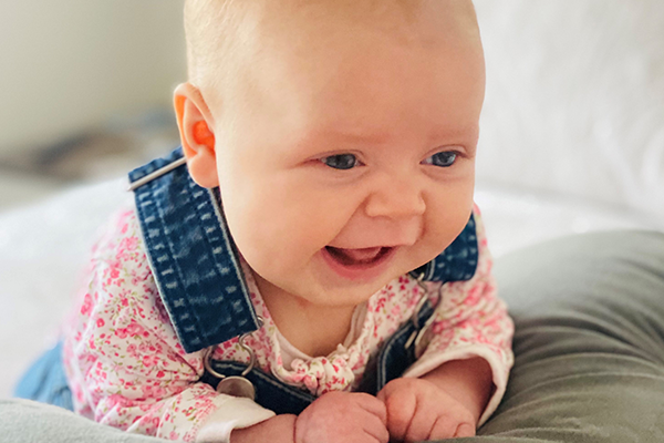 Baby Ava wearing a pink top and overalls smiling.